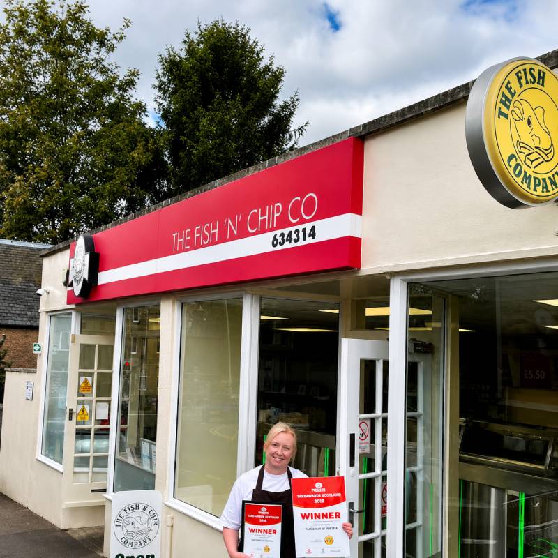 Staff member holding Mealzo award winner certificates outside The Fish 'N' Chip Co storefront in Perth.